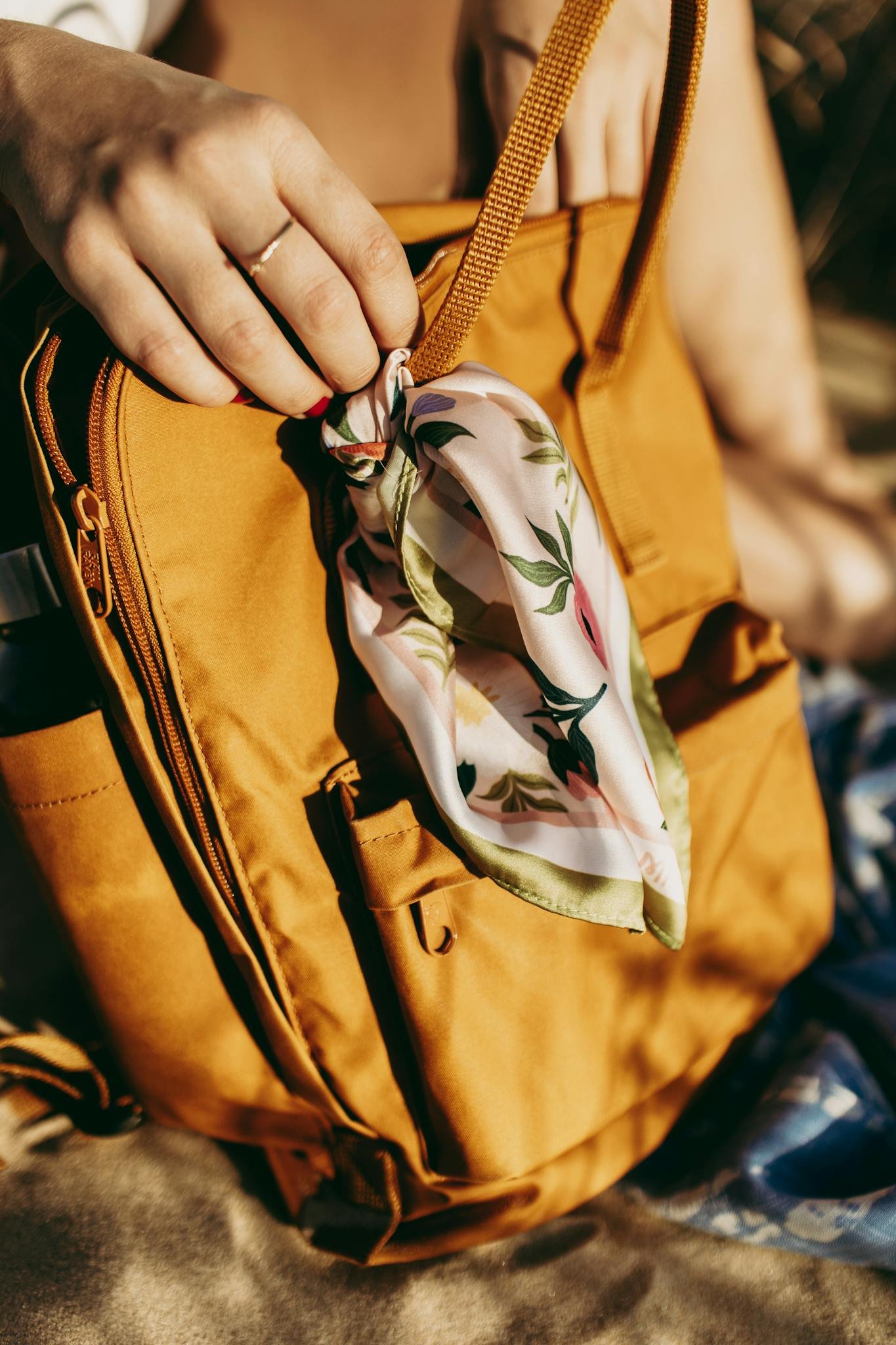 Crop unrecognizable female touching orange backpack with tied colorful scarf in sunny day